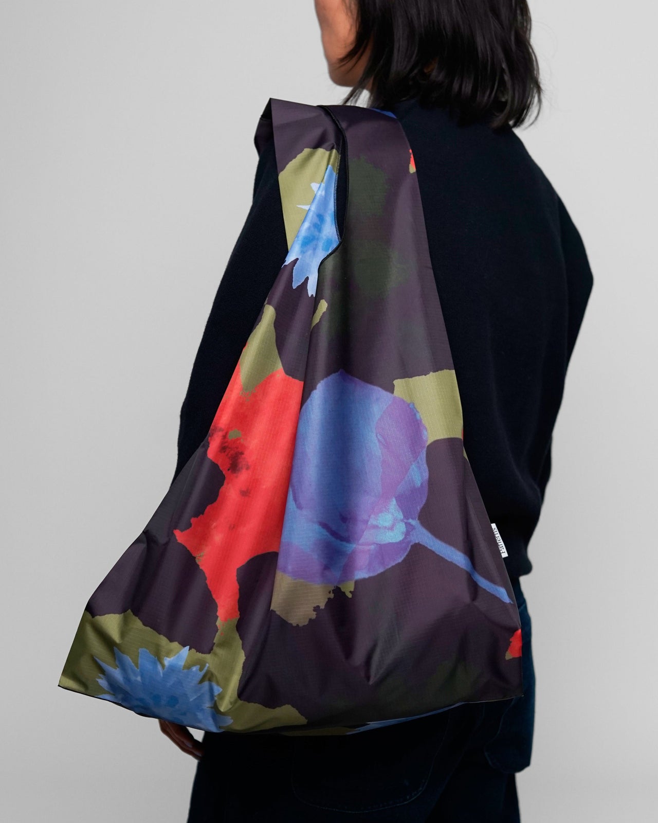 Person wearing a colorful floral-patterned bag on a plain background