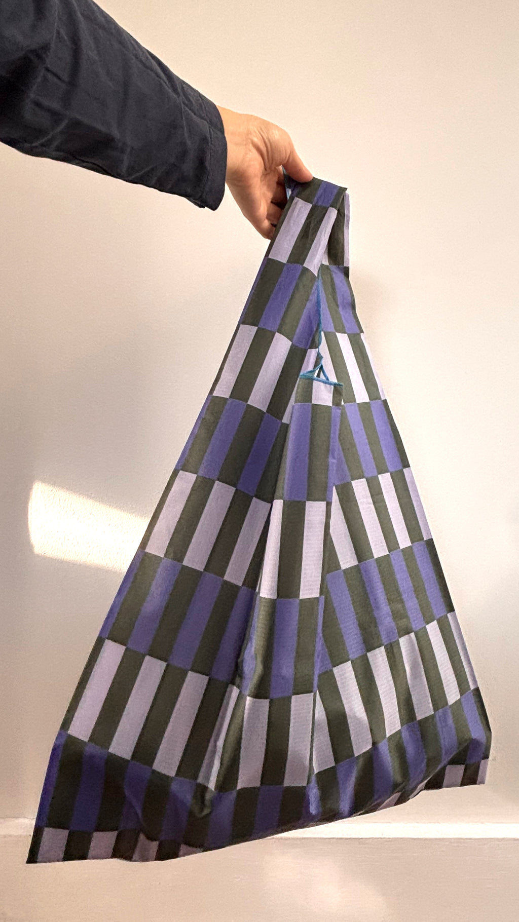 Person holding a patterned bag with geometric design on a neutral background