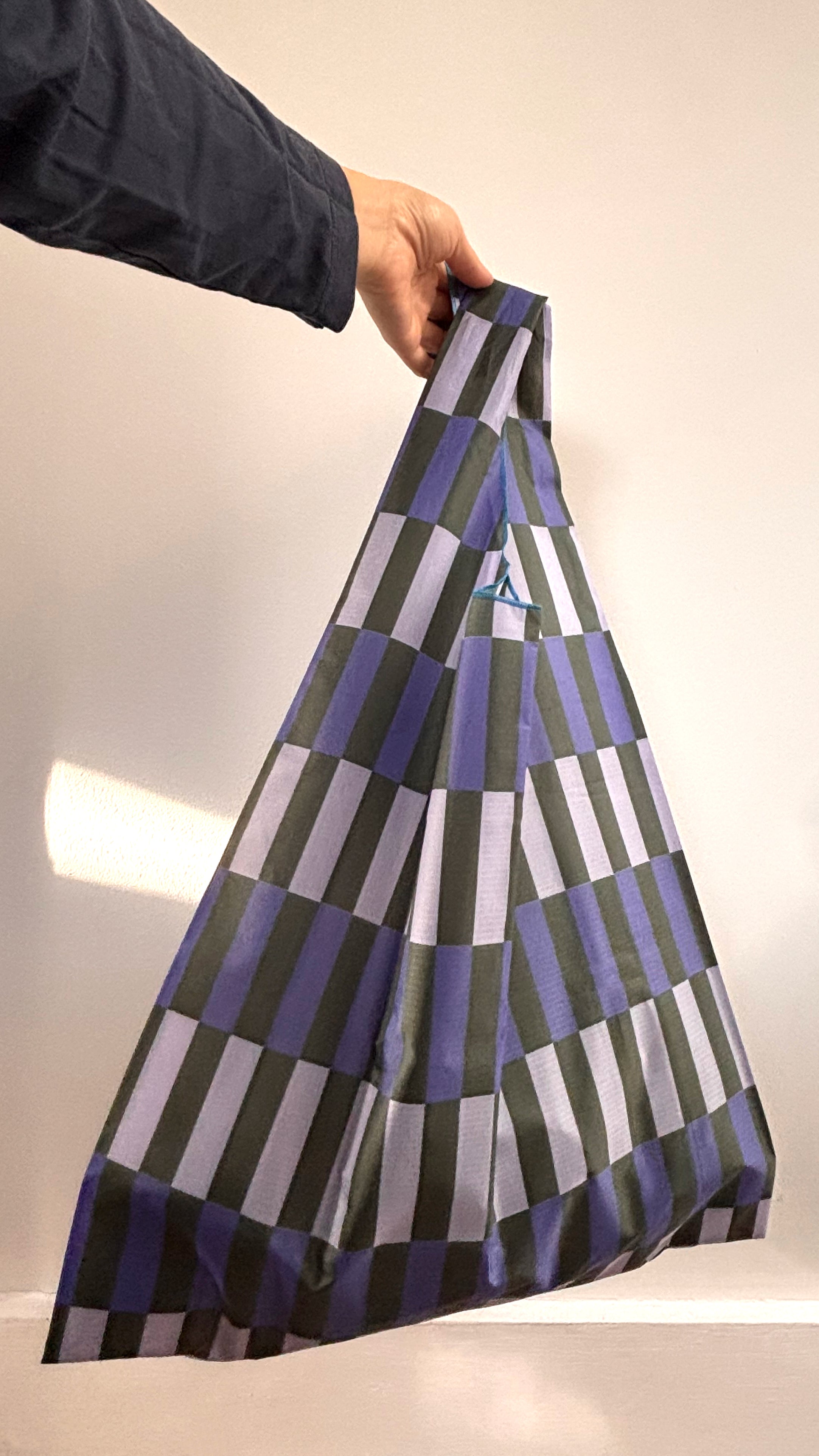 Person holding a patterned bag with geometric design on a neutral background