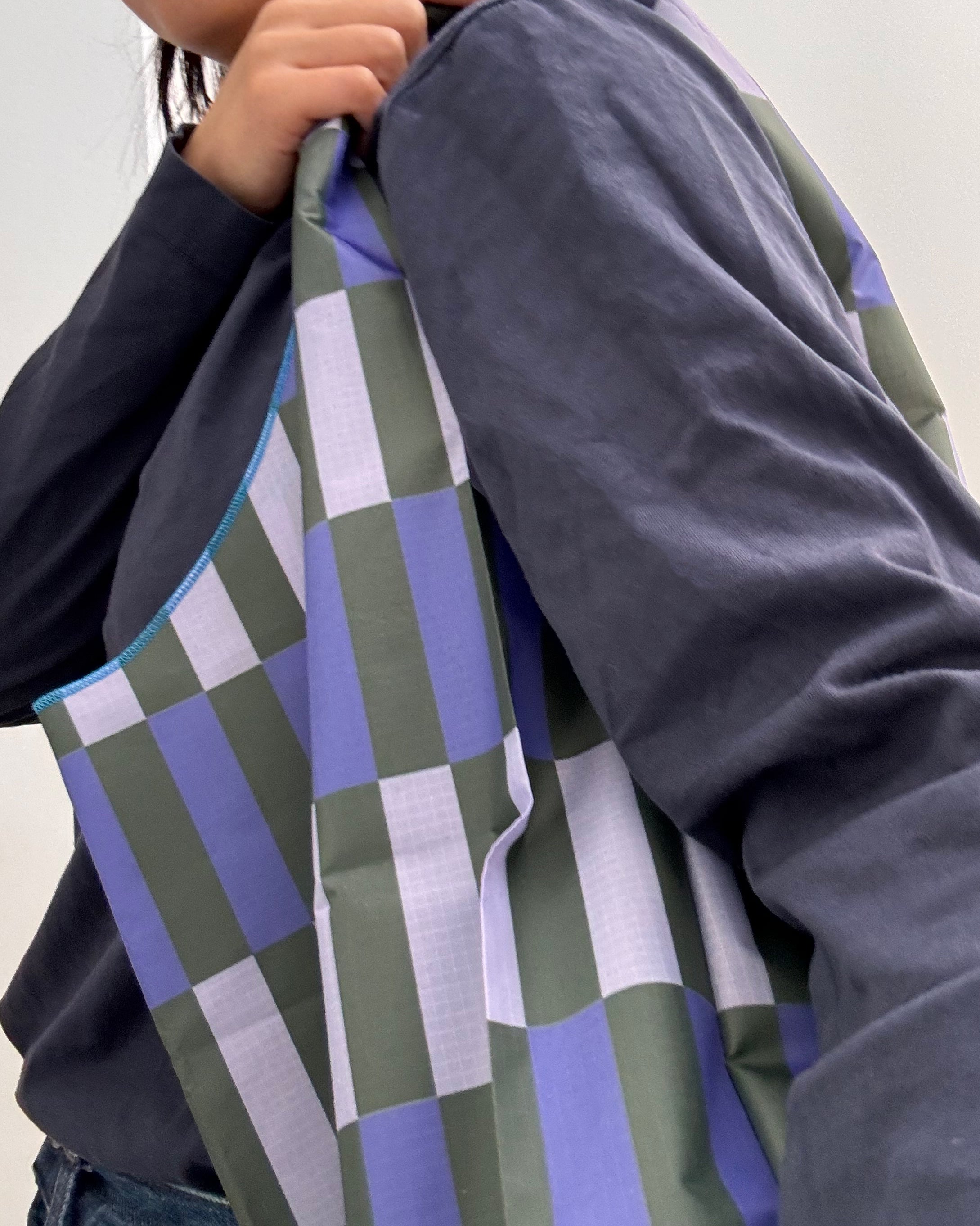 Person holding a geometric-patterned bag with blue, green, and gray colours over the shoulder.