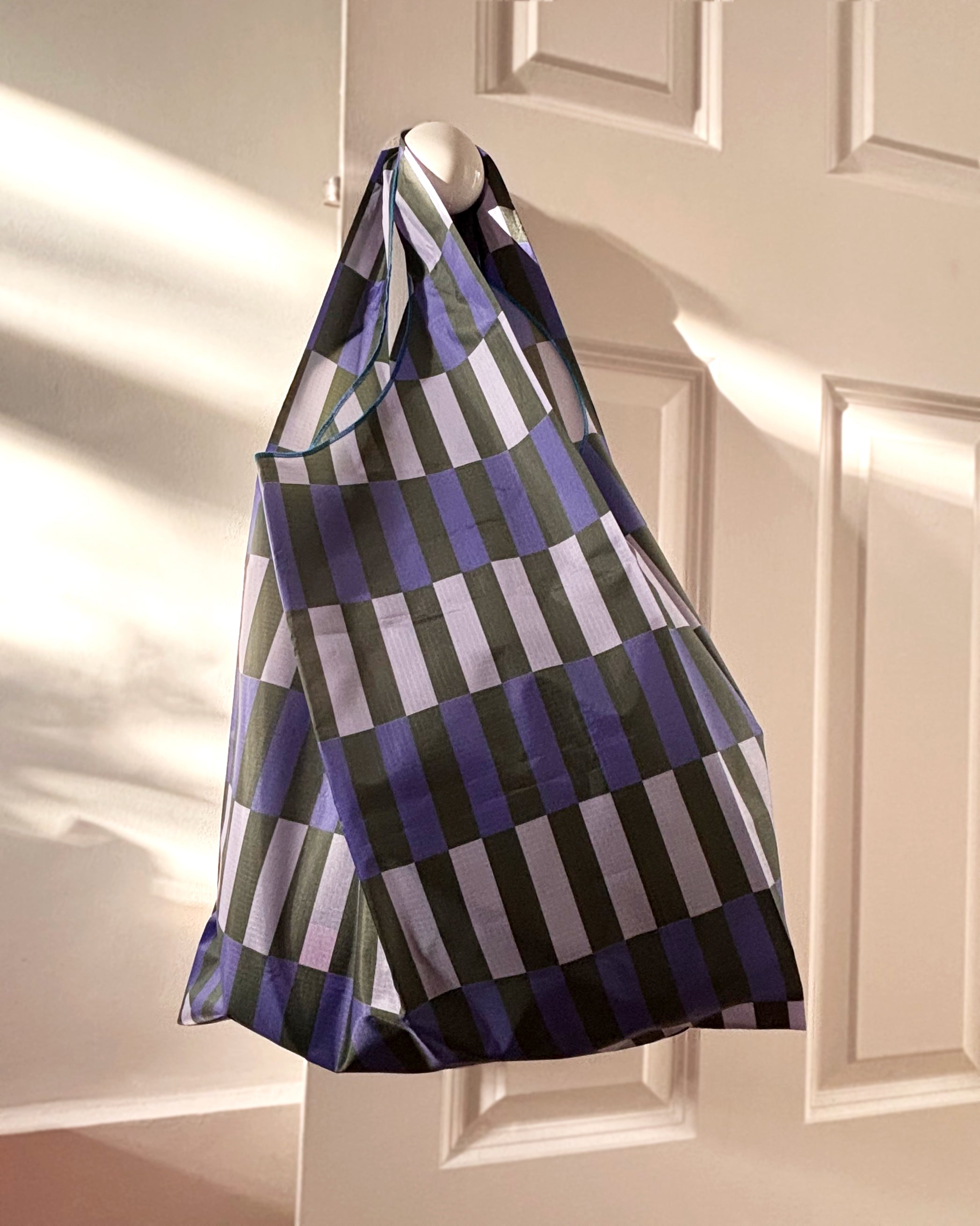 the Autumn Stripe bag in a cool colourway, hanging on a door handle, showing its scale and portability. 
