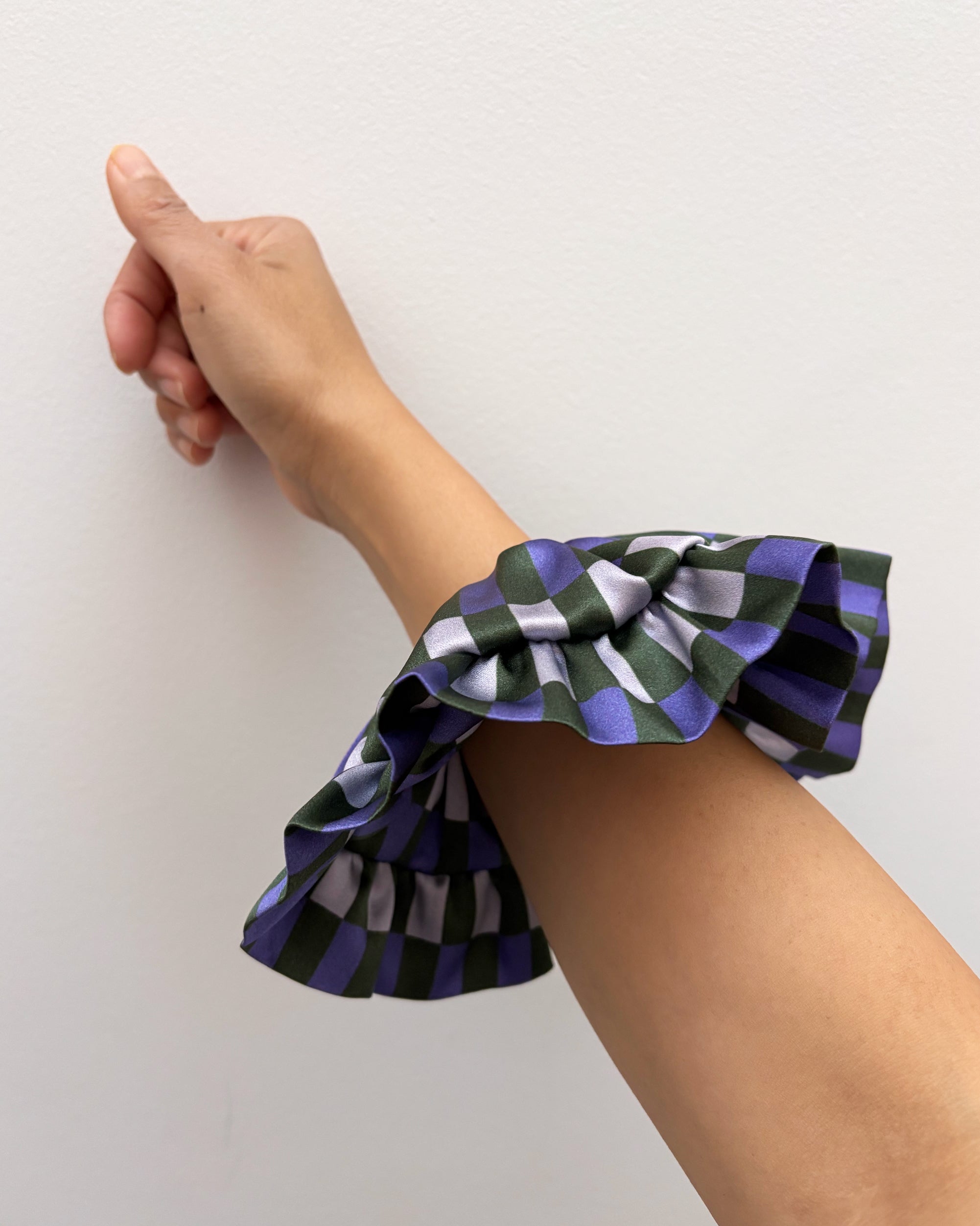 Hand wearing a colorful ruffled wristband on a plain background