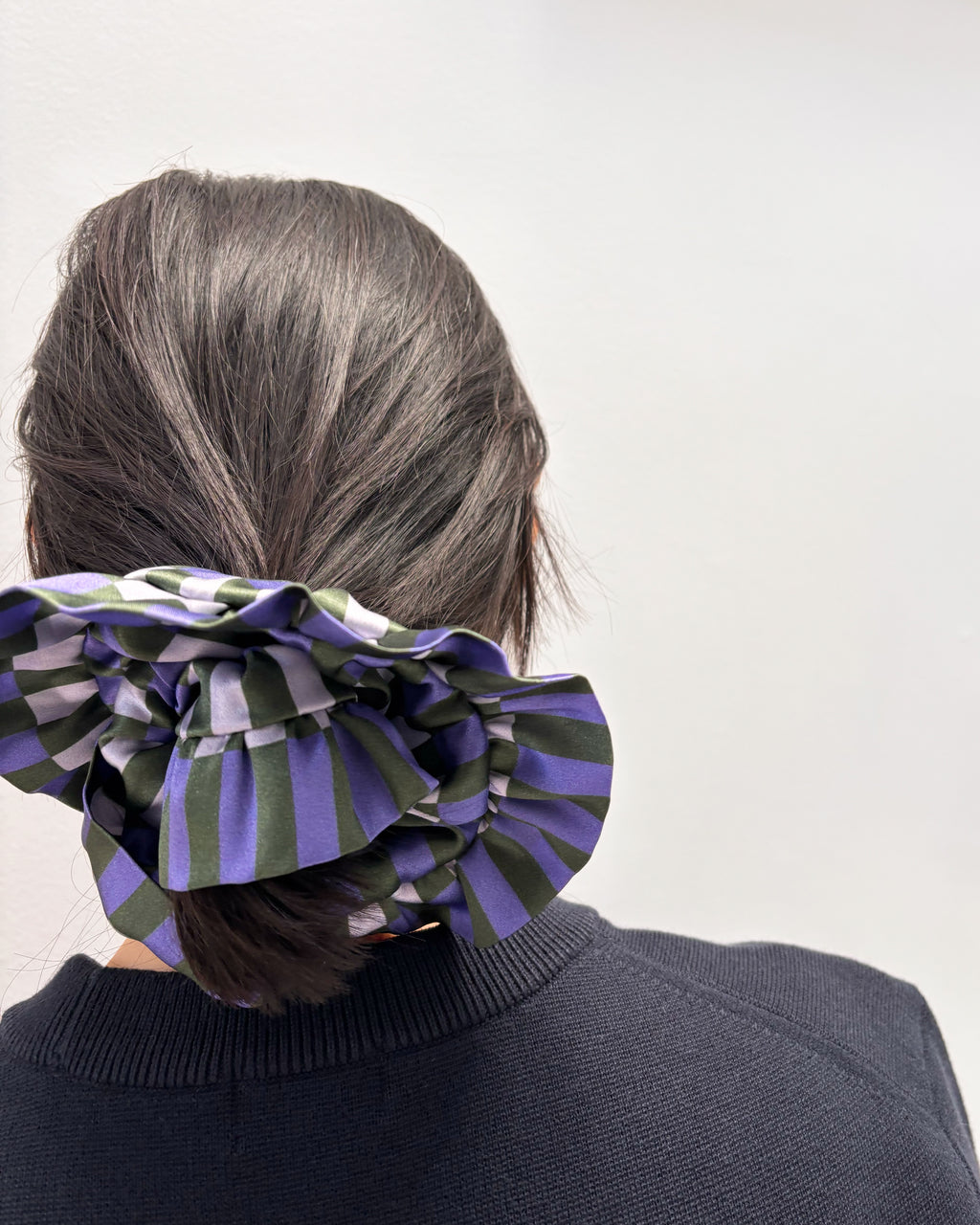 Person wearing a large striped hair scrunchie on a plain background