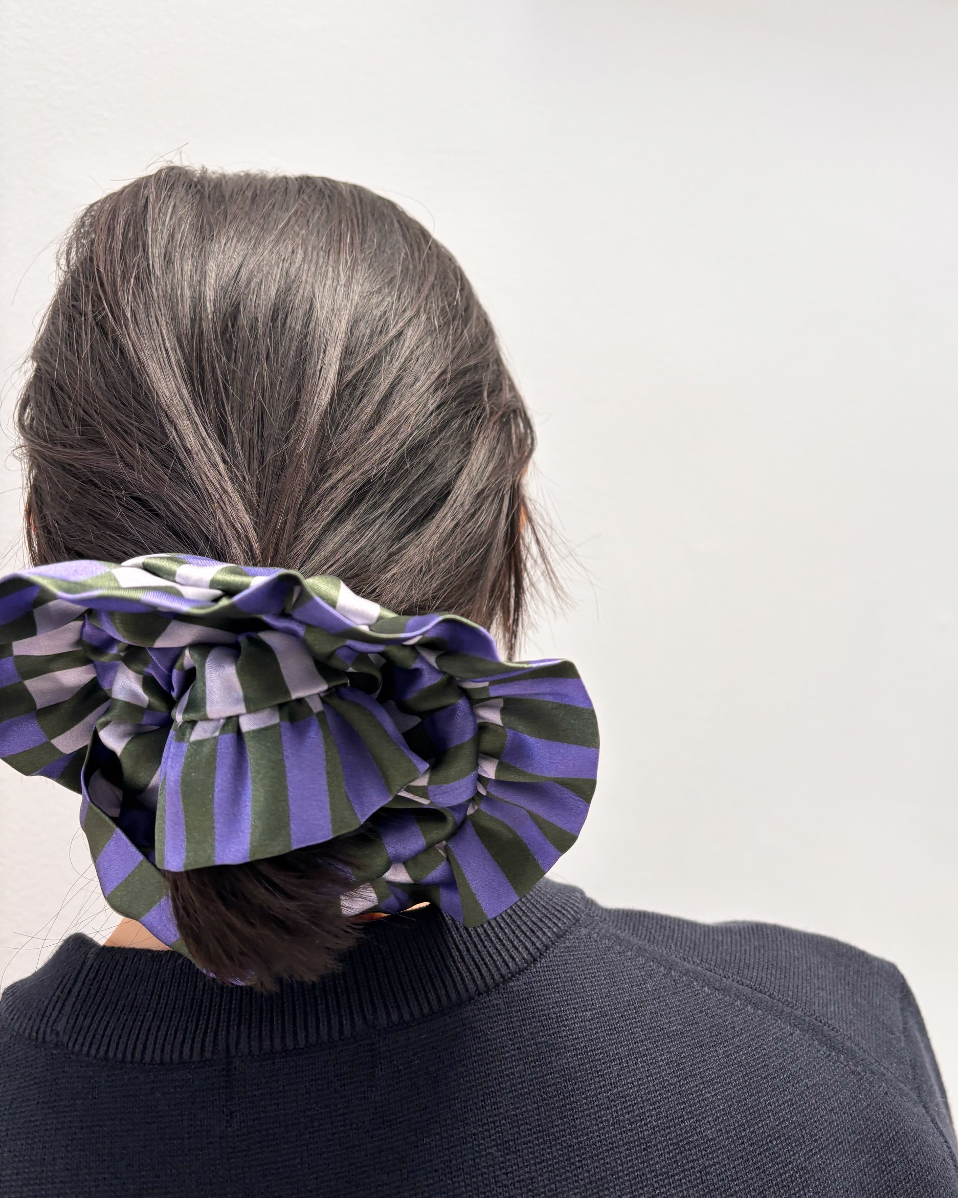 Person wearing a large striped hair scrunchie on a plain background