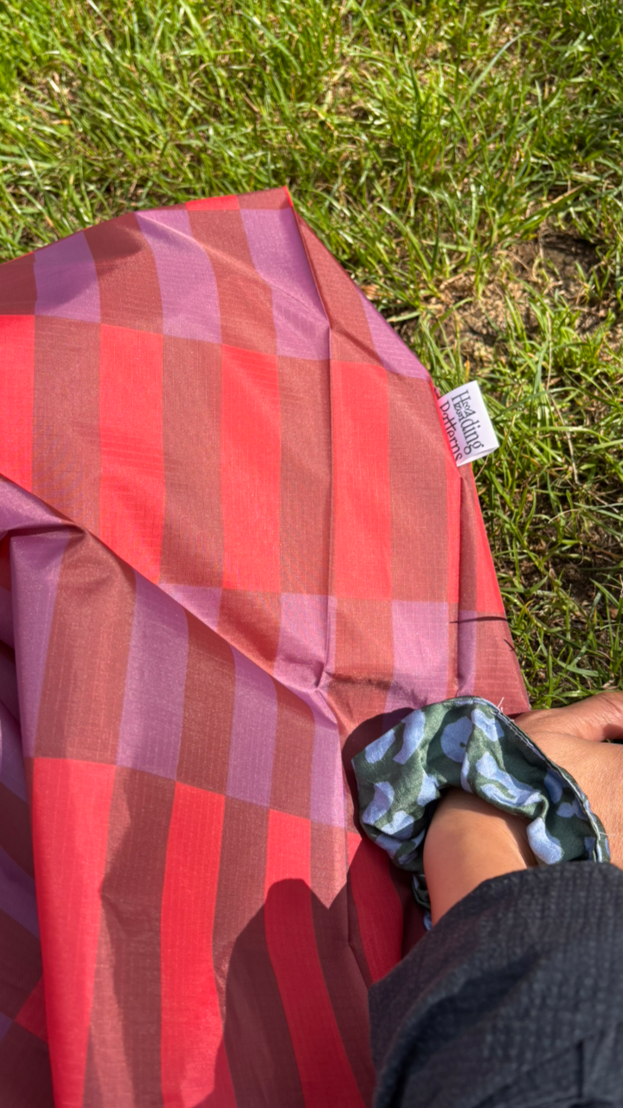 Red and purple plaid fabric on grass with a visible brand label.