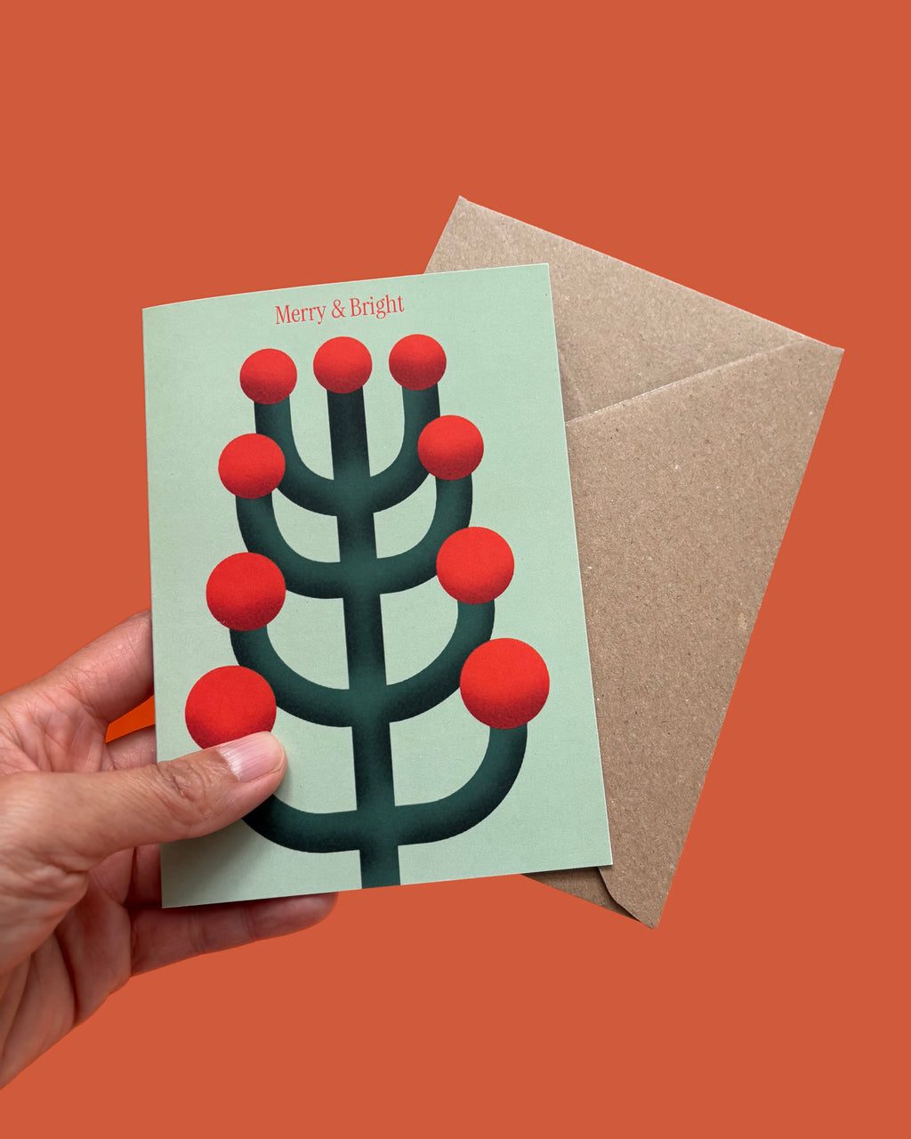Greeting card with red and green design held by a hand on an orange background