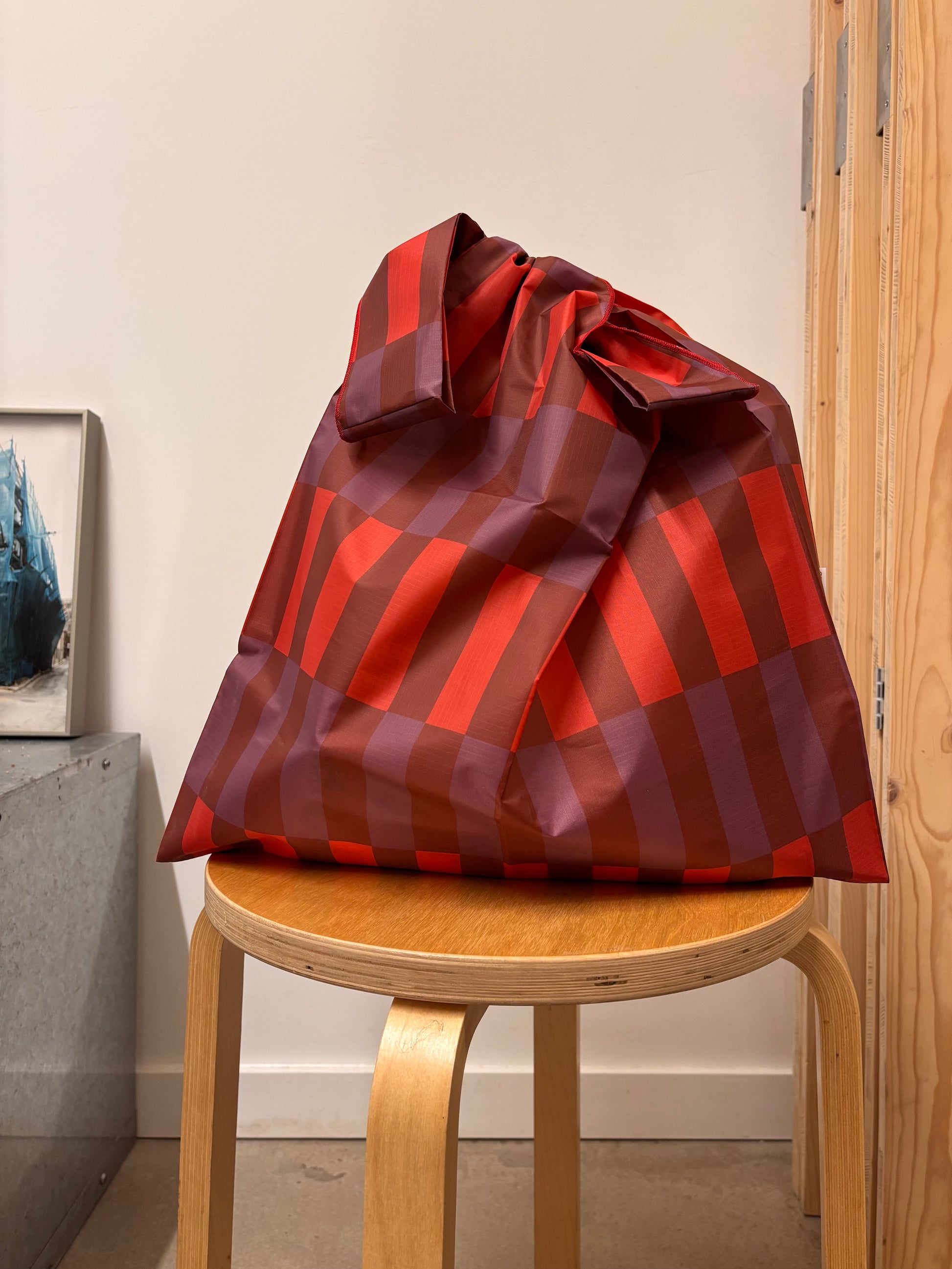 Red and brown striped gift bag tied with a bow on a wooden stool against a neutral wall.