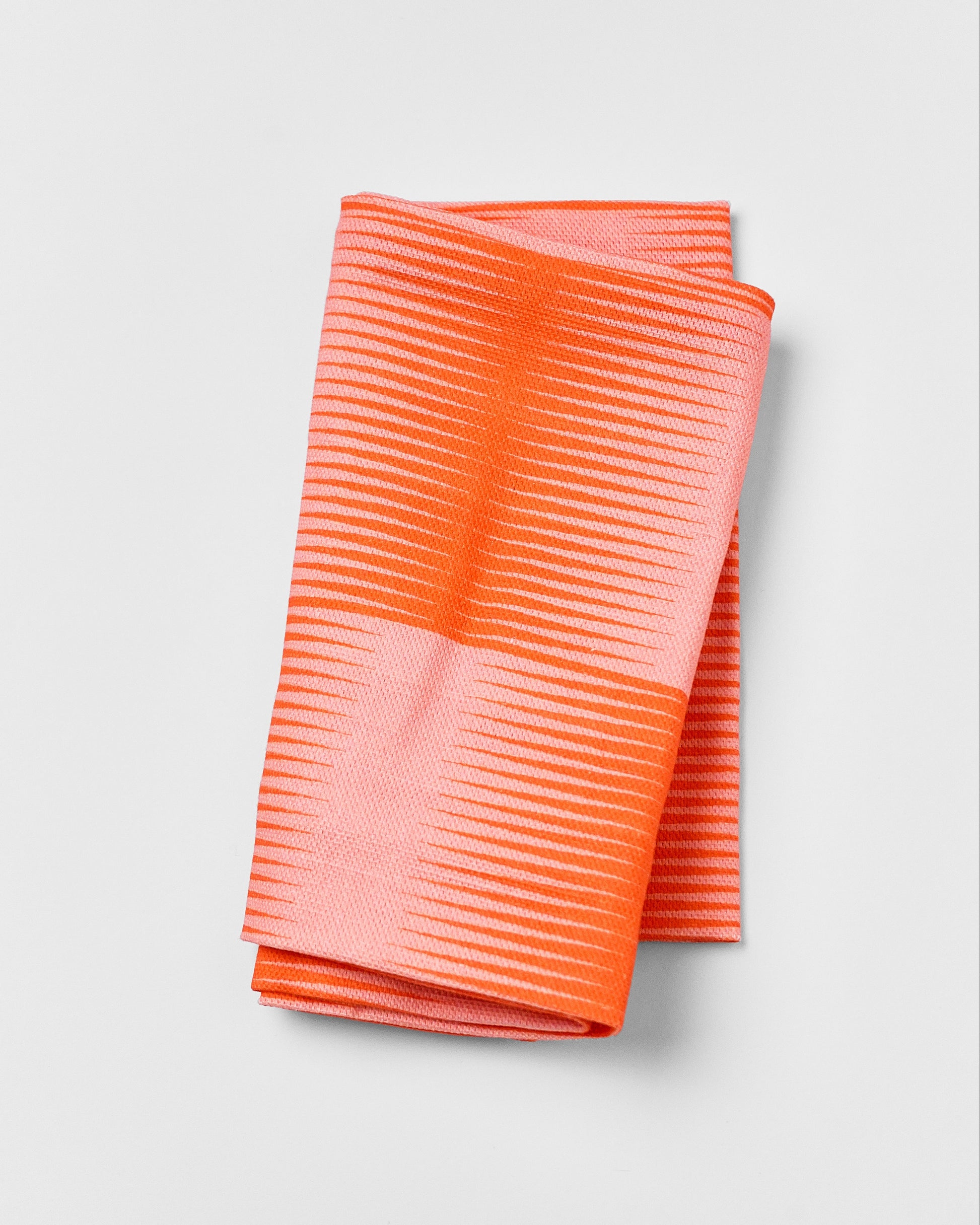 Folded orange patterned tea towel on a light gray background