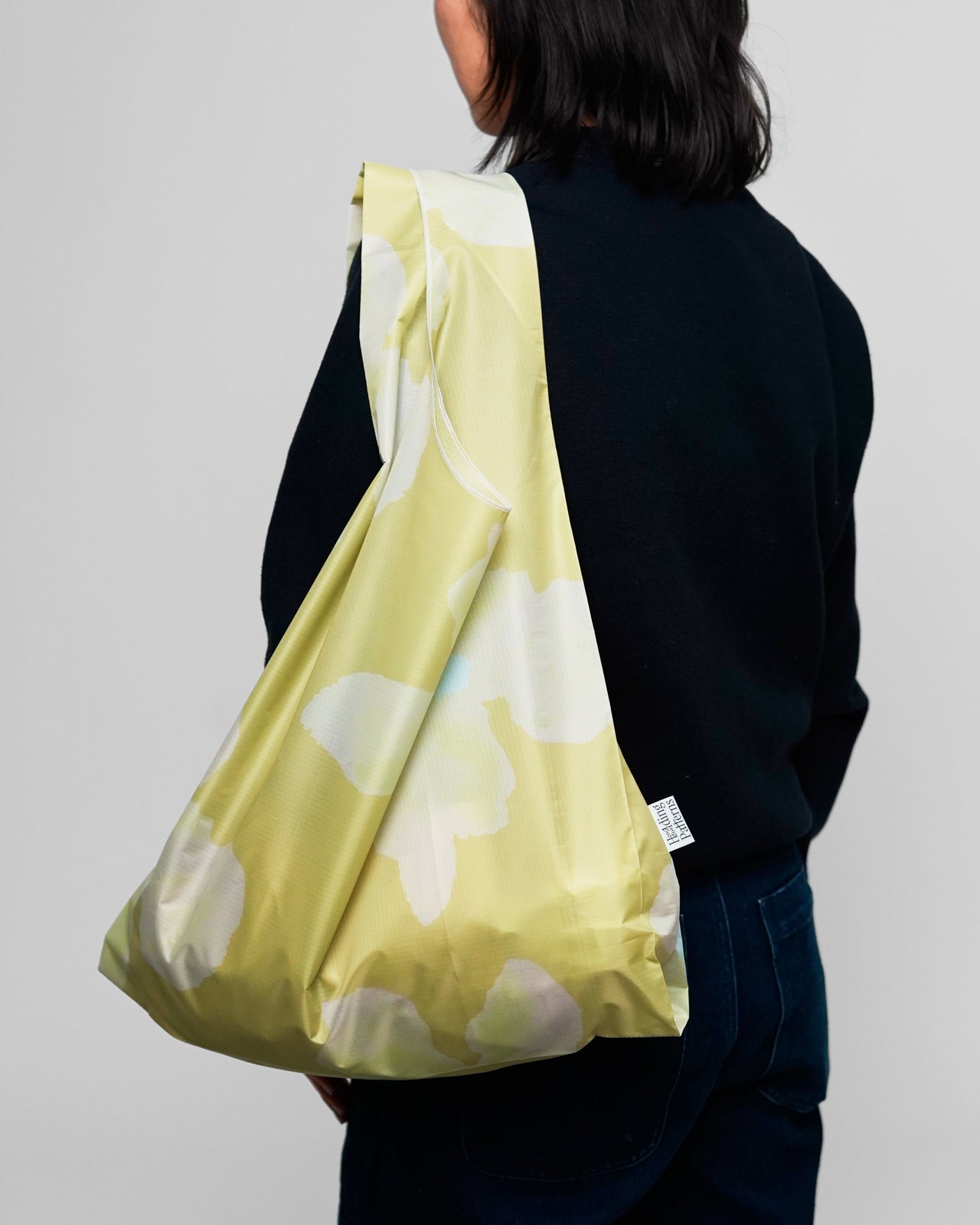 Person wearing a lemon yellow bag with watercolour floral print on a plain background