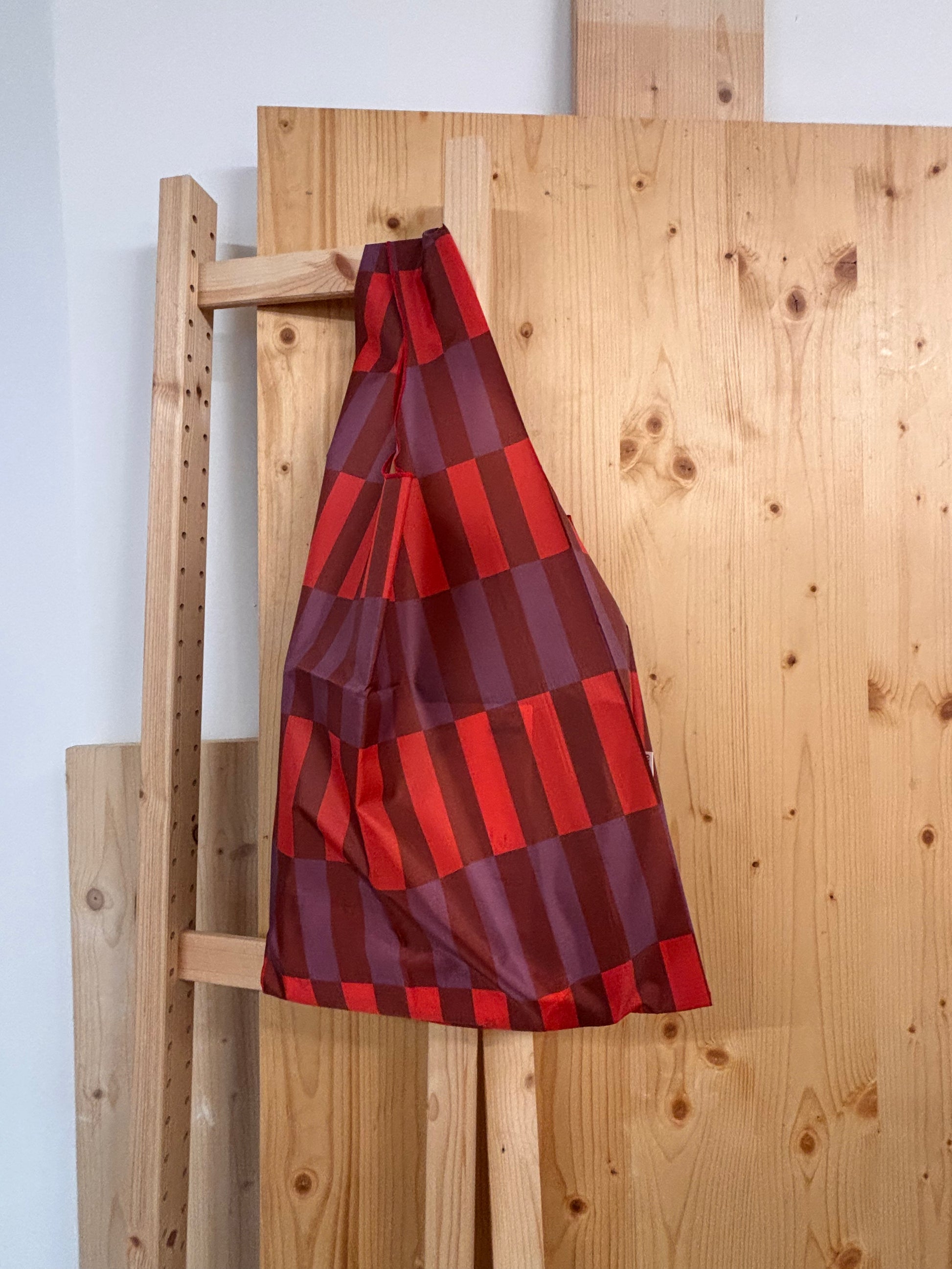 Red and purple checkered fabric draped over a wooden easel against a white wall.