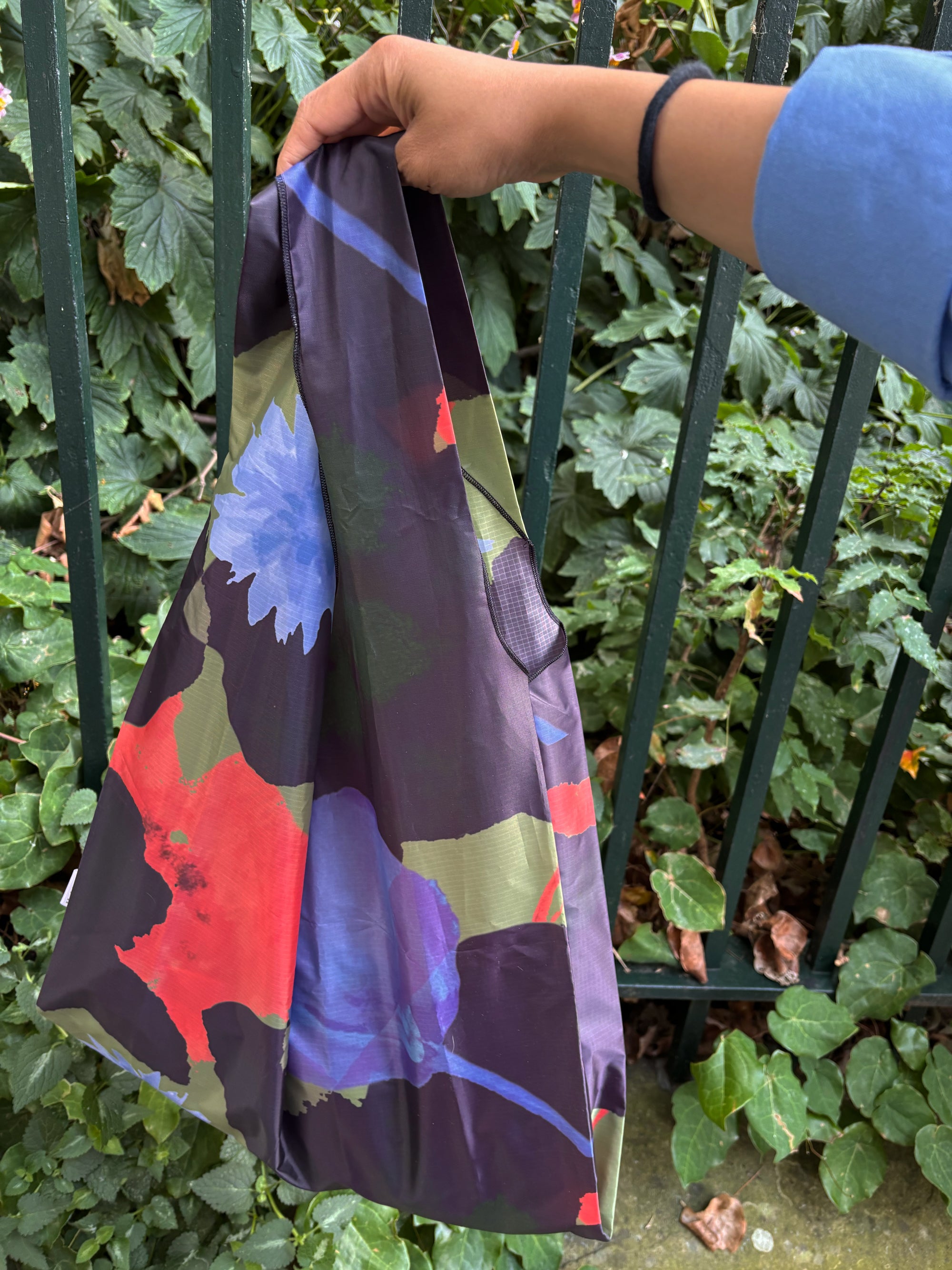 Colorful bag with abstract design held by a person against a green leafy background