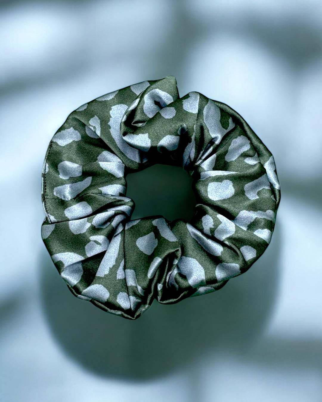 an oversize hair scrunchie made of 94% silk in a leopard print pattern and aubergine / lavender colourway on a high-gloss silk fabric background