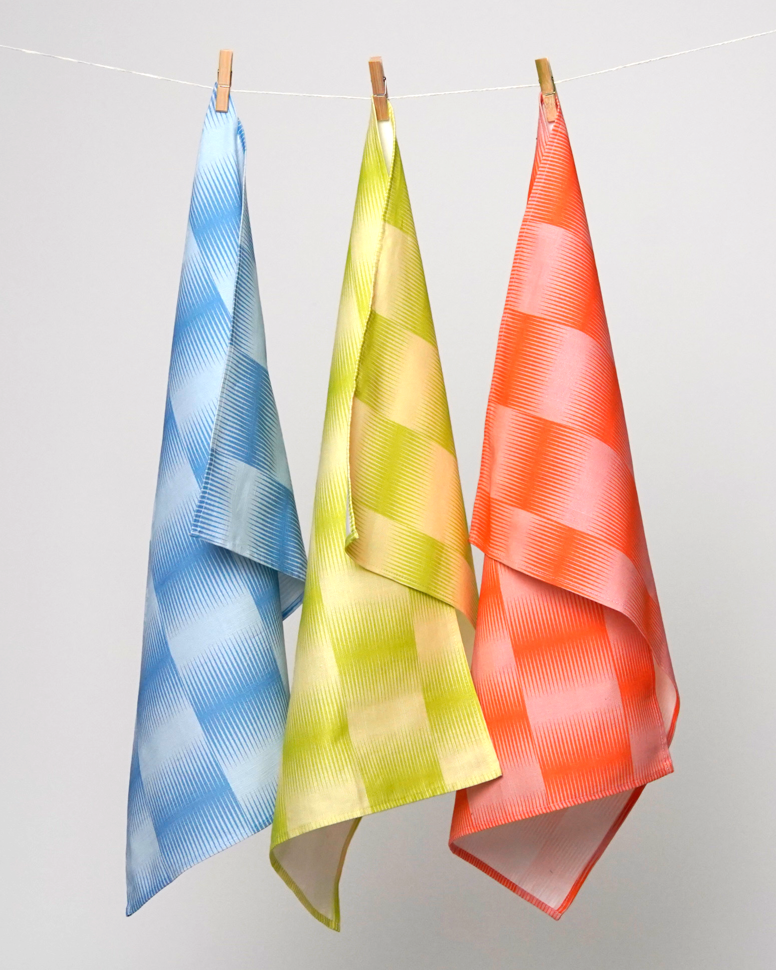 Three colorful towels hanging on a line against a light gray background