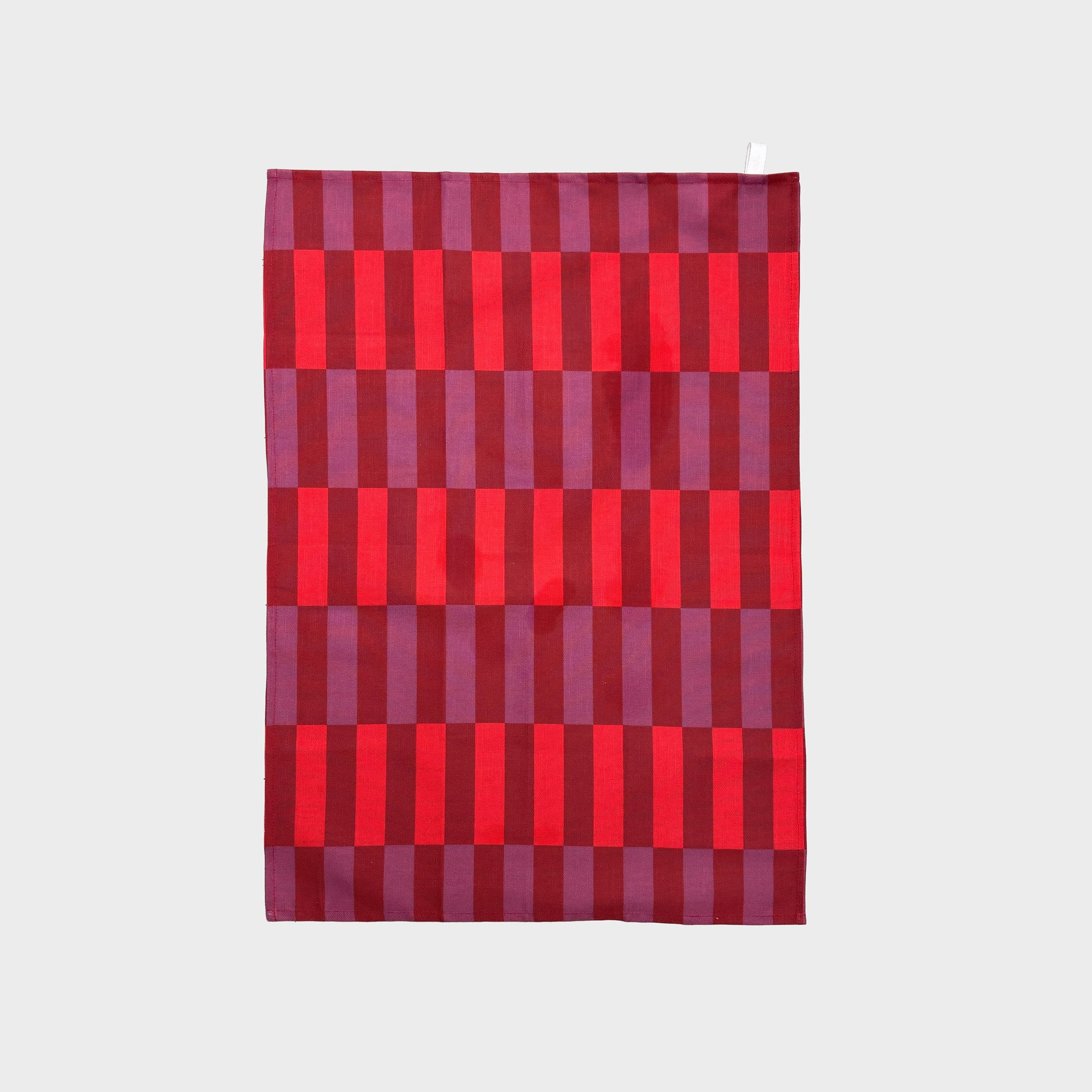 A rectangular textile item, likely a towel or blanket, featuring a geometric pattern of alternating red and purple vertical stripes in varying widths, shown flat against a light gray background.