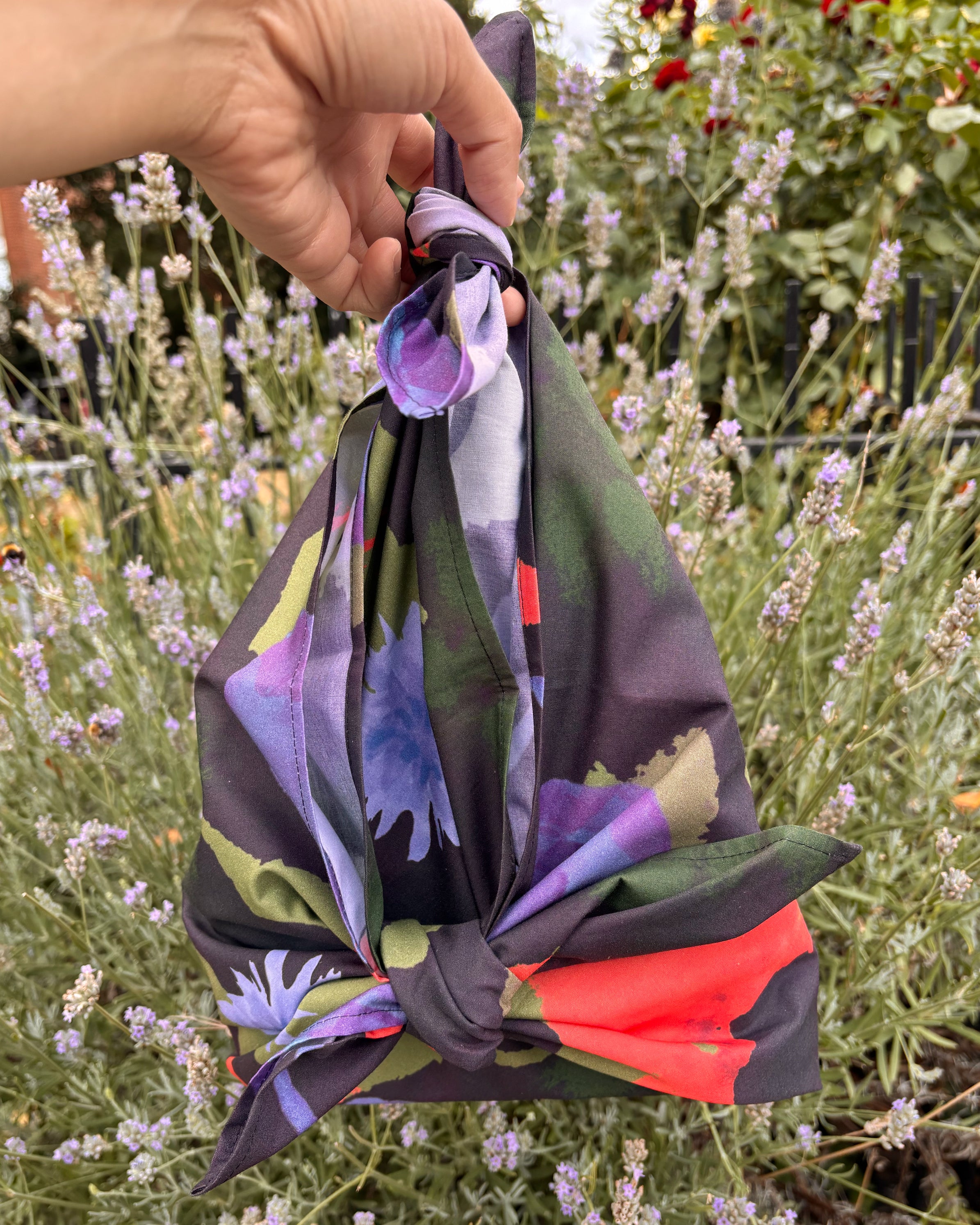 Colorful fabric with floral patterns held by a hand against a blurred natural background